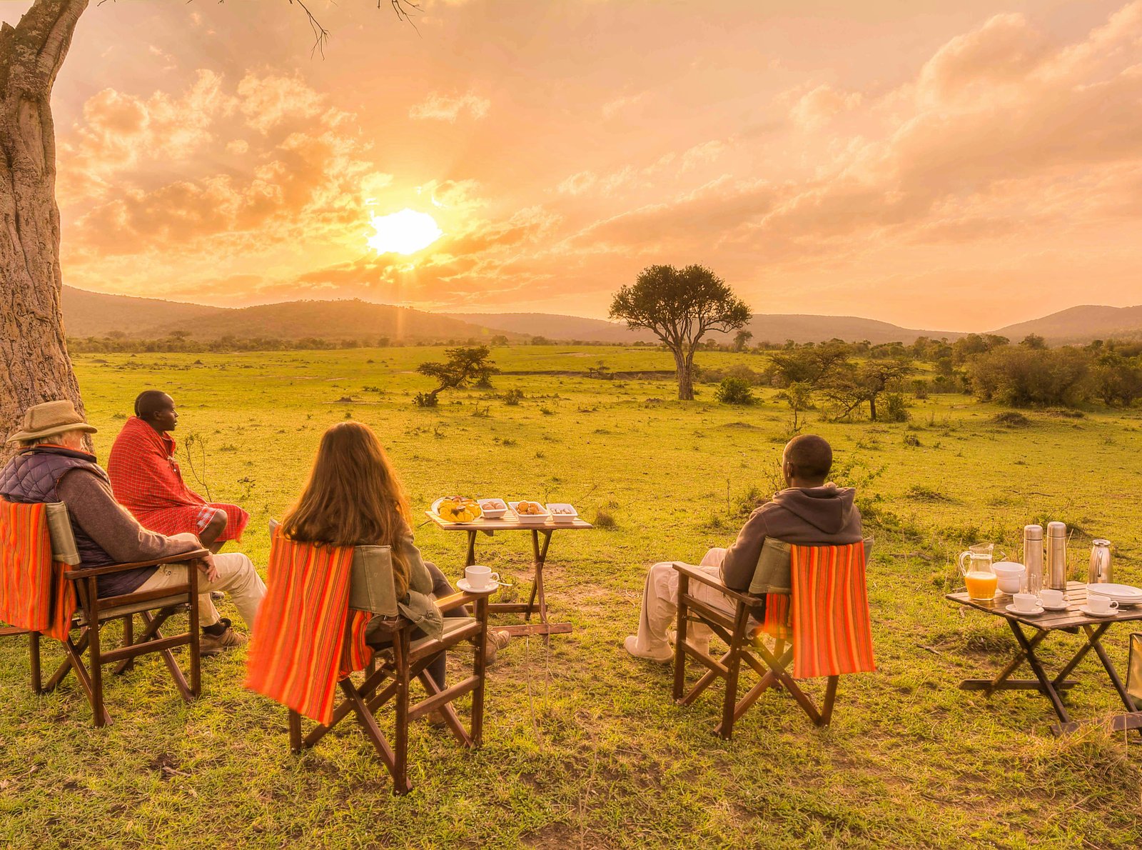 Couple enjoying sundowners by a lake with safari vehicle nearby